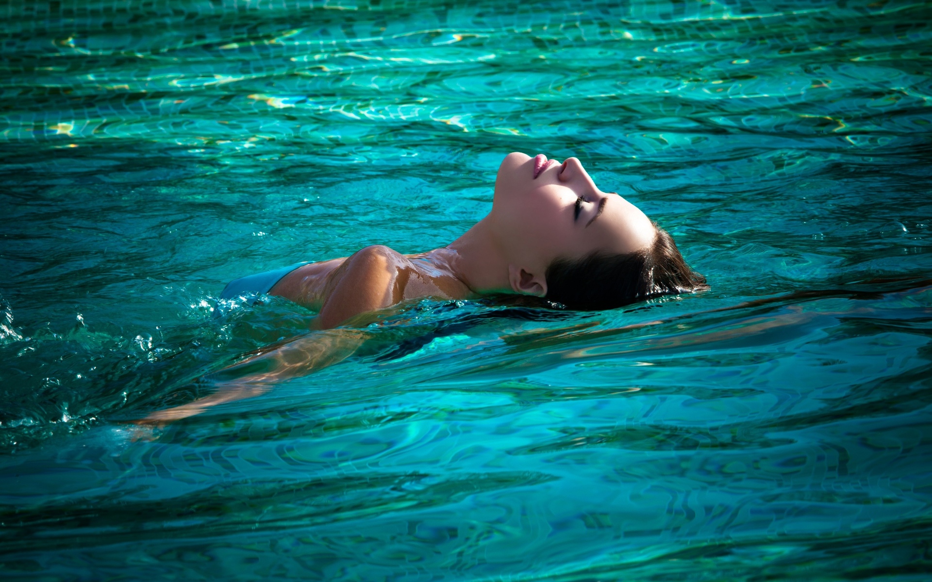 Красивая брюнетка в зеленом купальнике плавает на надувном матрасе в море